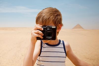 Un enfant prend une photo dans le désert devant les pyramides de Gizeh - Egypte