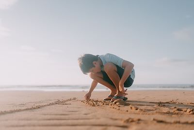 Un enfant dessine sur le sable 