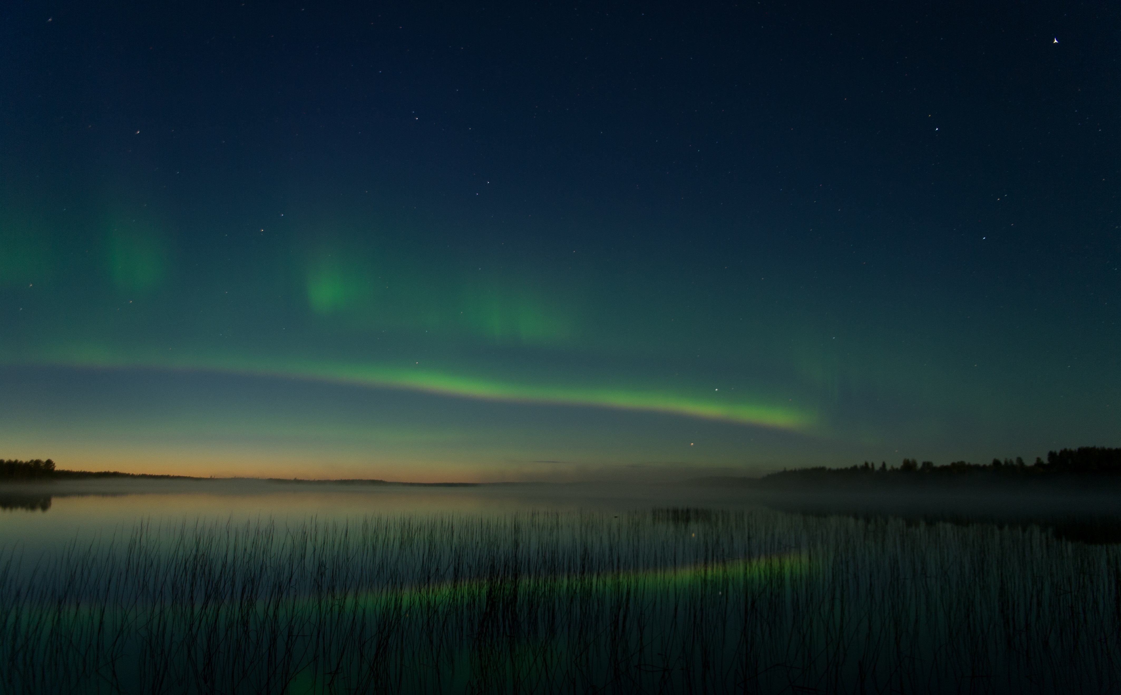 Une aurore boréale brille au loin au-dessus d'un des nombreux lacs de Finlande ©Sabrina Logeais / Taïga Spirit